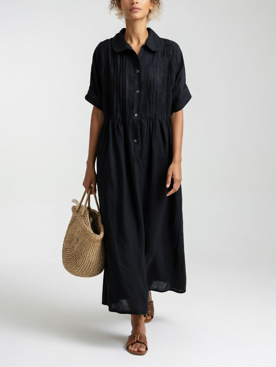 Model in the black dress facing front, carrying a woven straw tote, showing dark buttons and the gathered waistline. 7