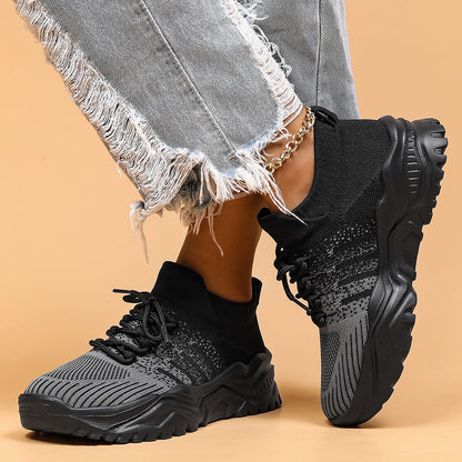Black and grey knit lace-up sneakers with thick black soles, worn by a model in distressed jeans and a gold anklet. 2