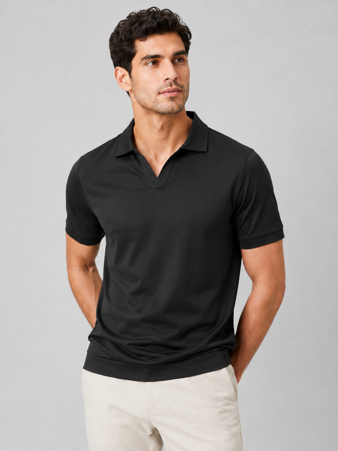Model wearing the black polo with a V-neck collar and ribbed hem, front view in a studio, paired with cream trousers. 6