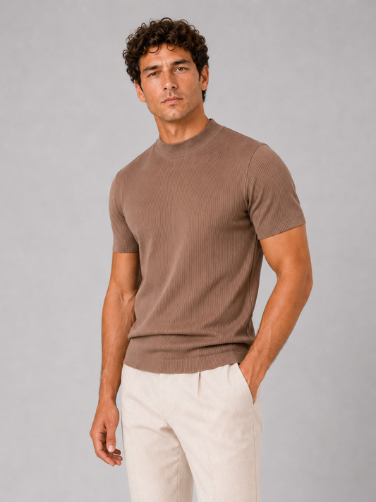 Model in a brown ribbed mock neck top with cream pleated trousers, three-quarter front view against grey backdrop. 1