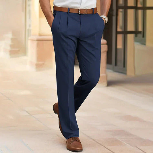 Model walking outdoors in navy pleated trousers with a brown leather belt, white shirt and tan lace-up shoes. 1