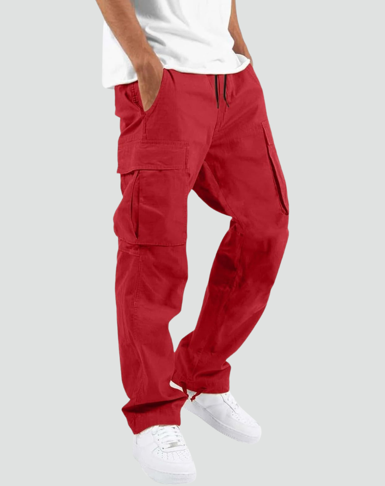 Model wearing red cargo trousers with drawstring waist and large side flap pockets, with white t-shirt and trainers, on a grey background. 10