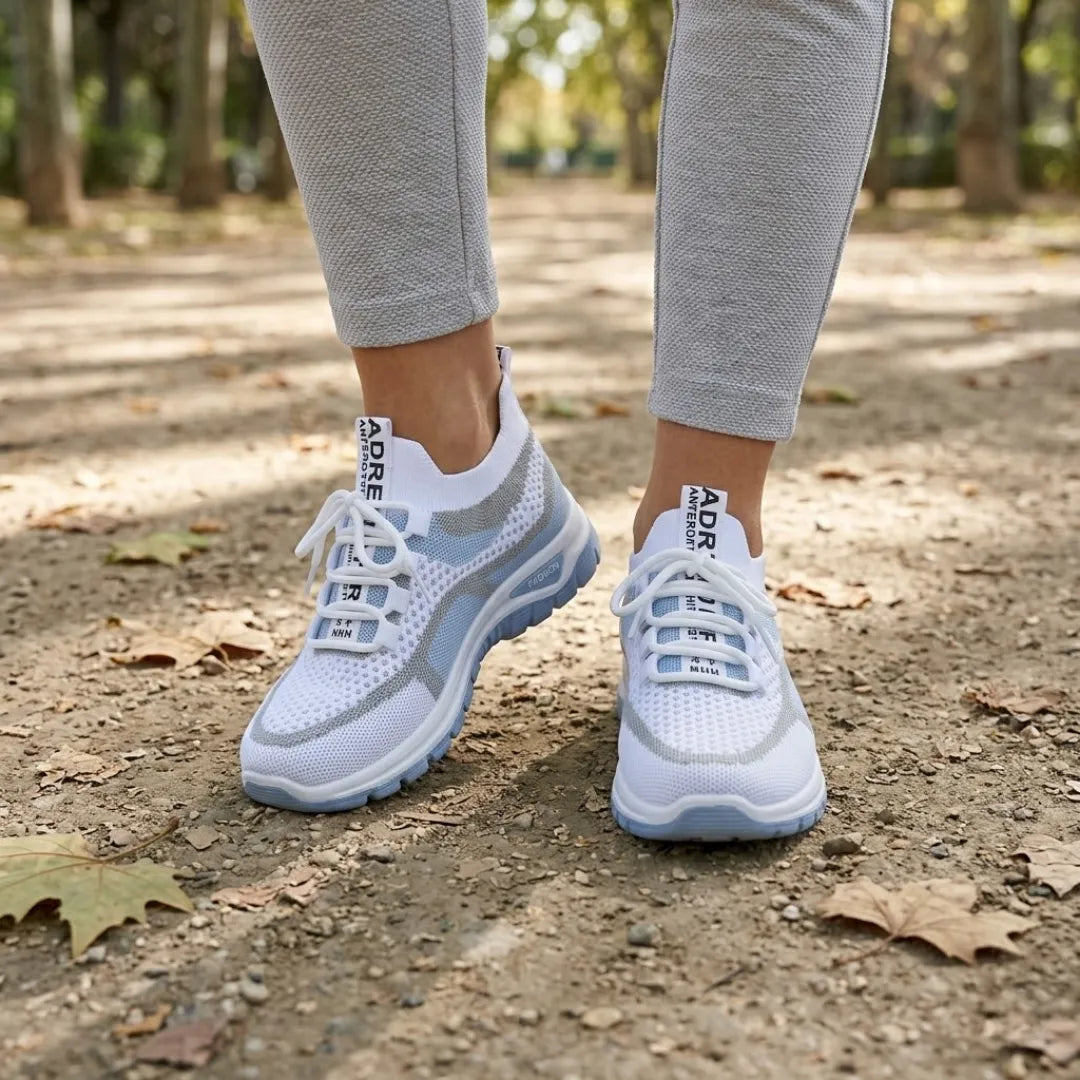 Pair of white and pale blue mesh trainers worn with grey leggings, walking on a leaf-strewn park path. 2