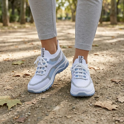 Pair of white and pale blue mesh trainers worn with grey leggings, walking on a leaf-strewn park path. 2
