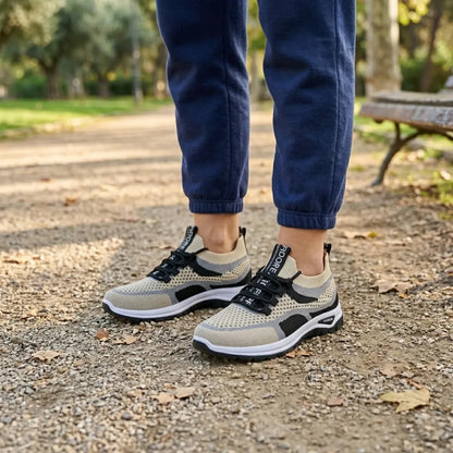 Woman's feet in beige, grey and black mesh trainers standing on a park path, wearing navy joggers, bench and trees behind. 38
