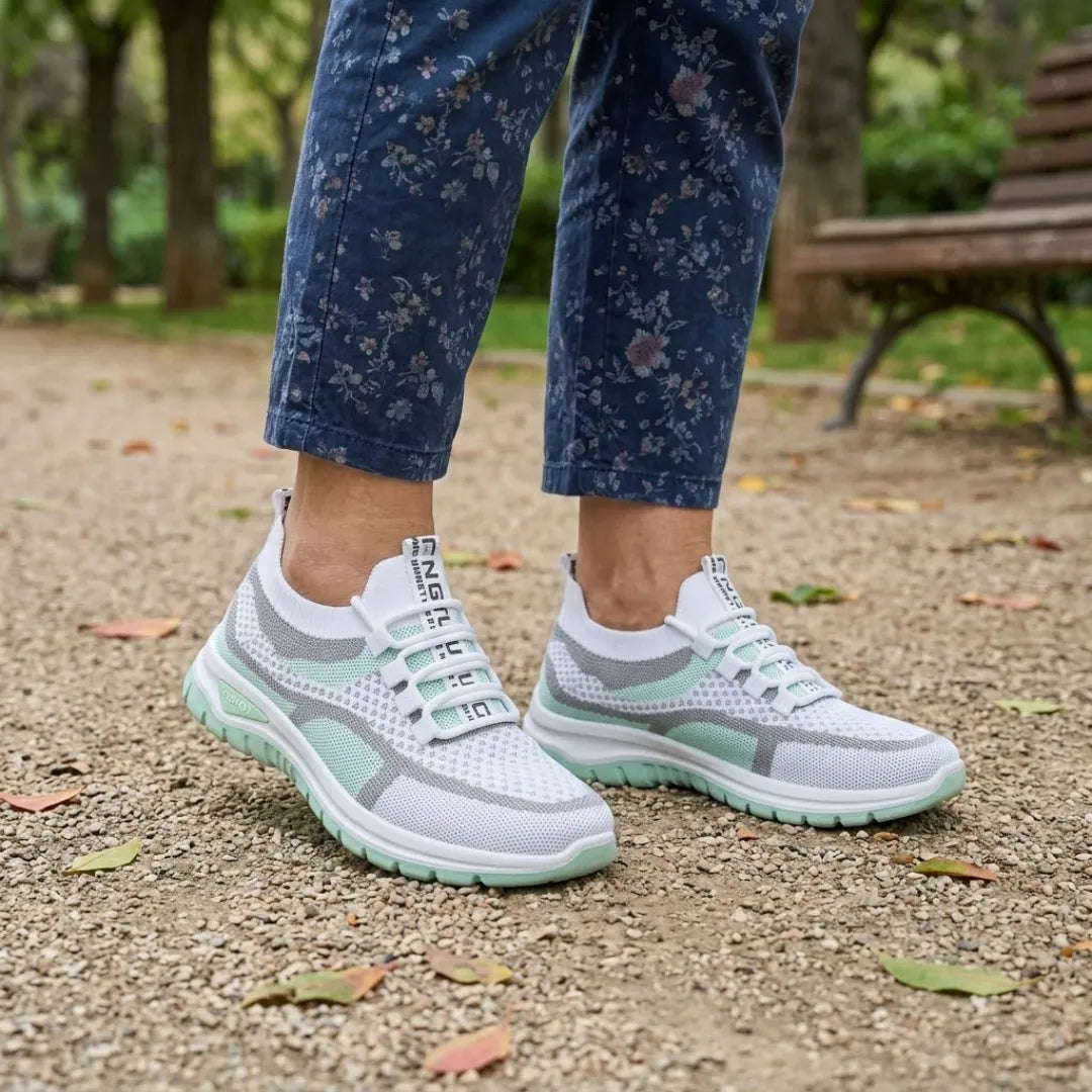 Pair of white and mint green mesh trainers worn with floral navy trousers on a gravel park path. 11