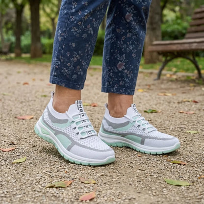 Pair of white and mint green mesh trainers worn with floral navy trousers on a gravel park path. 11