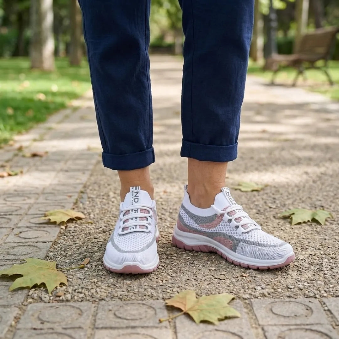 Pair of white and pink mesh trainers worn with rolled navy trousers on a paved and gravel park path. 20