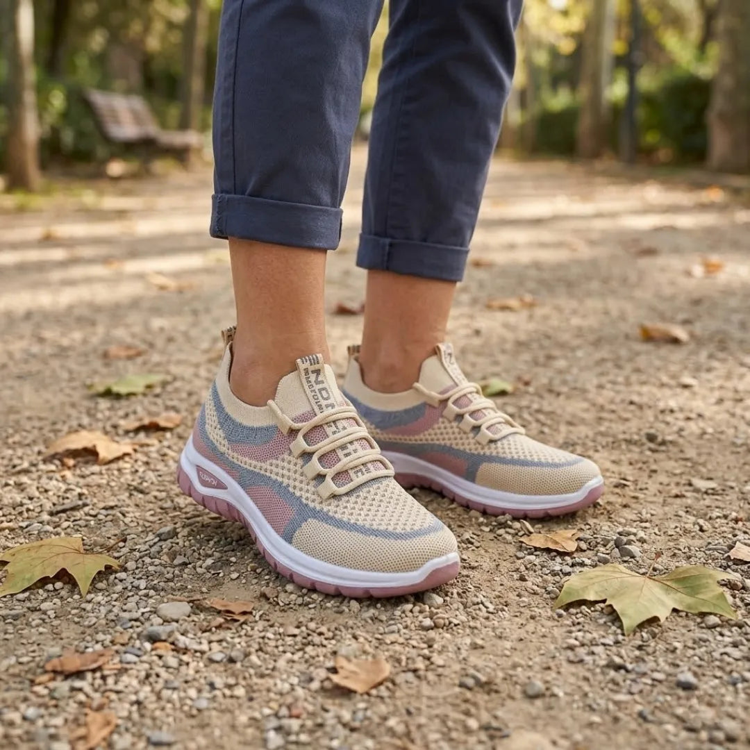 Woman's feet in beige, pink and grey mesh trainers walking on a park path scattered with autumn leaves, wearing rolled navy trousers. 29