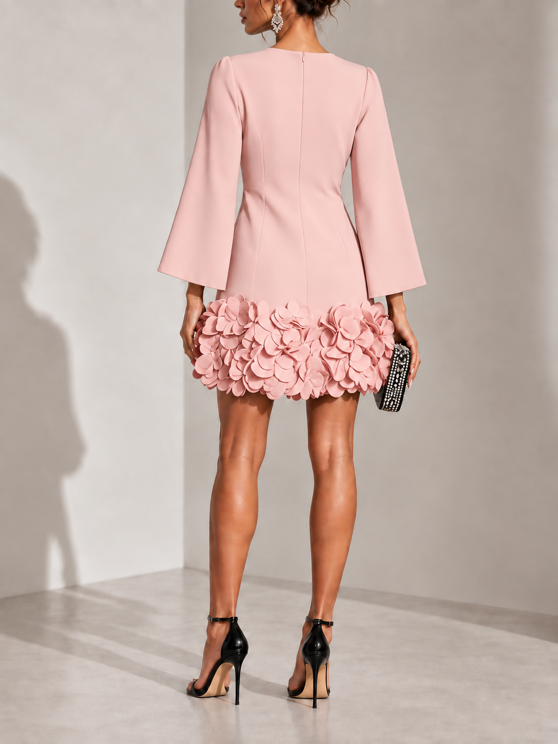 Back view of the dusty pink dress with centre zip, flared sleeves and a ruffled petal hem, worn with black heels. 10