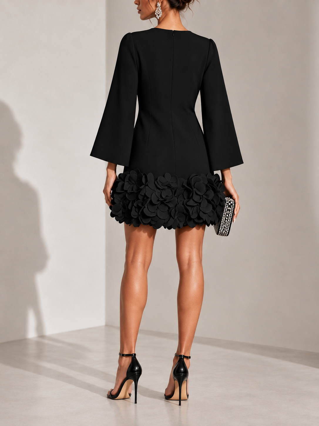 Back view of the black dress with a centre zip, flared sleeves and a hem of layered fabric petals. 3