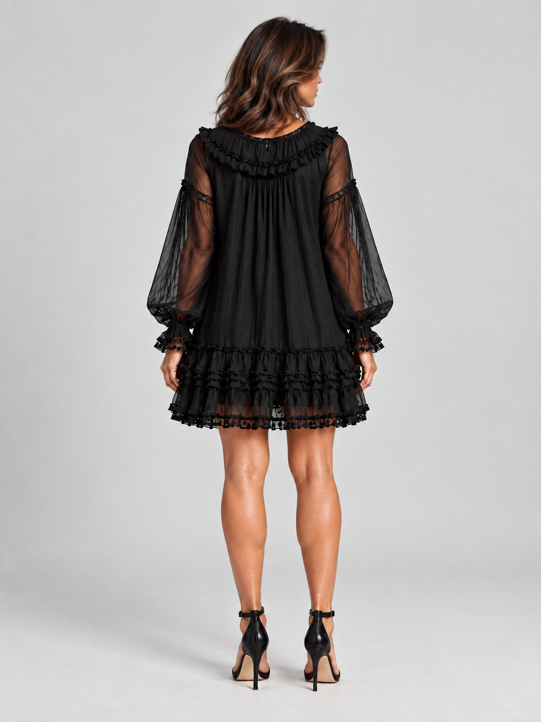 Back view of a model in the black dress, showing the ruffled round back neckline, gathered fabric and tiered lace-trimmed hem. 4