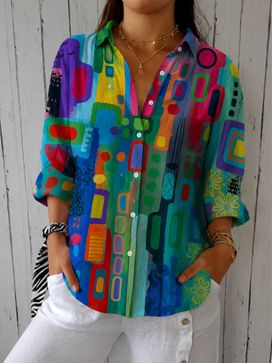 Front view of the blouse worn by a model in a bright multicoloured abstract print of blues, greens, reds and purples, with a collar. 2