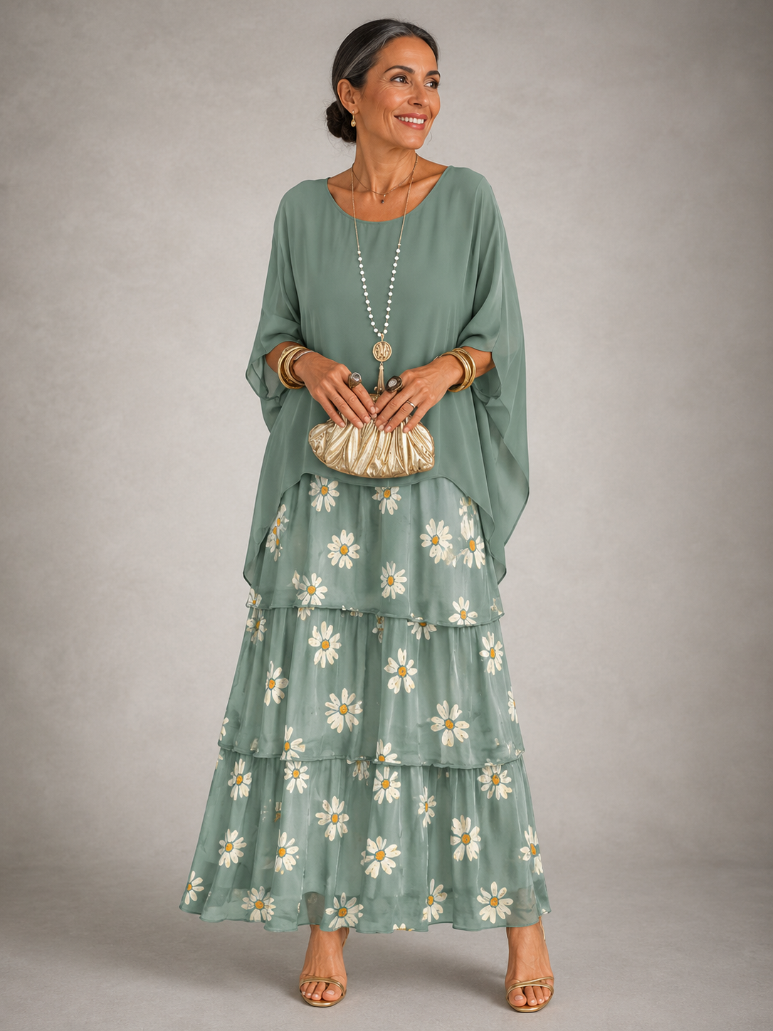 Woman in a sage green cape top over a tiered maxi skirt printed with white daisies, holding a gold clutch. 8