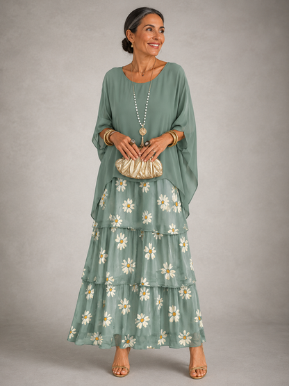 Woman in a sage green cape top over a tiered maxi skirt printed with white daisies, holding a gold clutch. 8