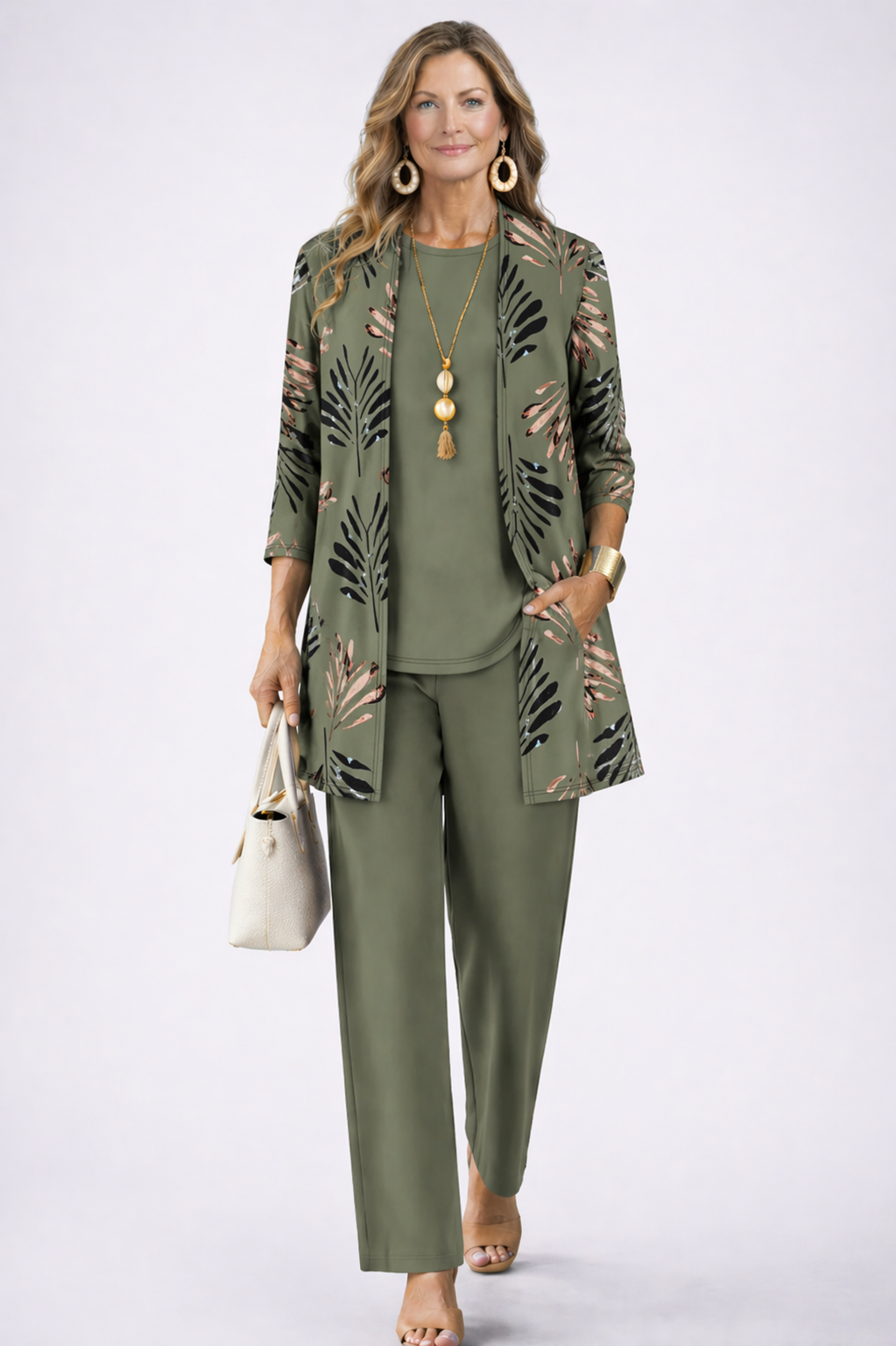 Model in an olive green set with a palm-leaf print open cardigan, holding a cream handbag 1