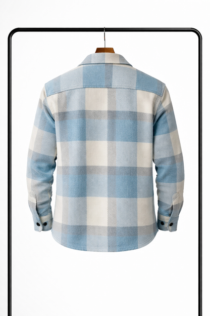 Back view of the pale blue, cream and grey check overshirt on a wooden hanger, showing the yoke and buttoned cuffs. 2