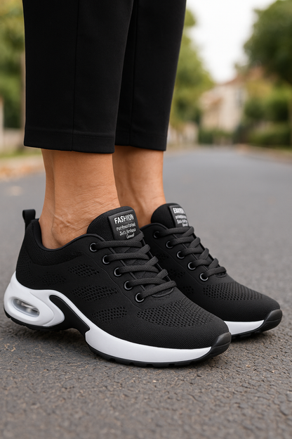 Black knit trainers with white air-cushion soles, worn with black trousers on an empty tree-lined road. 6