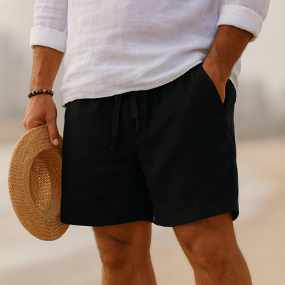 Black drawstring shorts with a stitched hem, worn on a beach with a white linen shirt, hand in pocket, straw hat in hand. 14