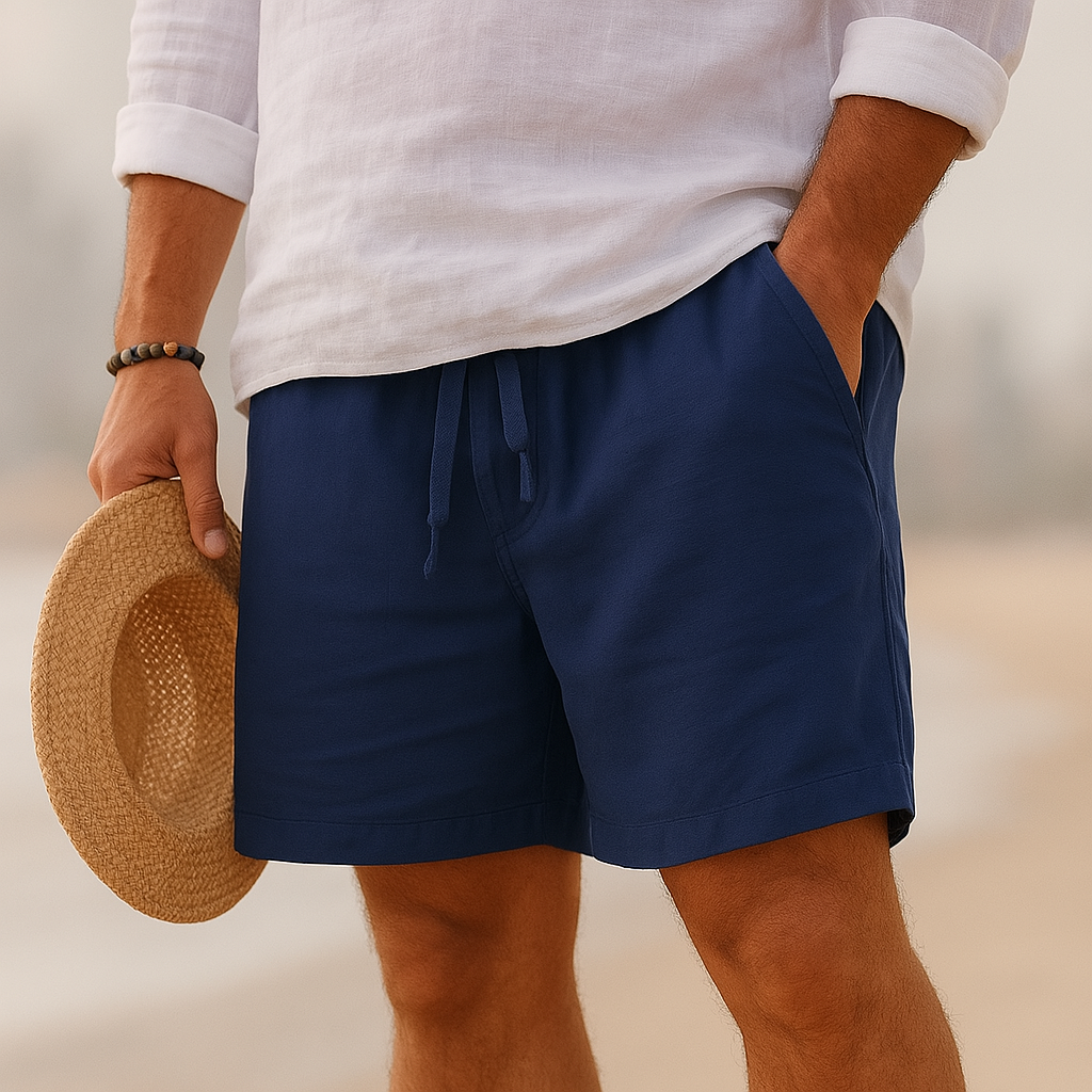 Navy blue drawstring shorts with stitched hem, worn on a beach with a white linen shirt and a straw hat held by the brim. 13