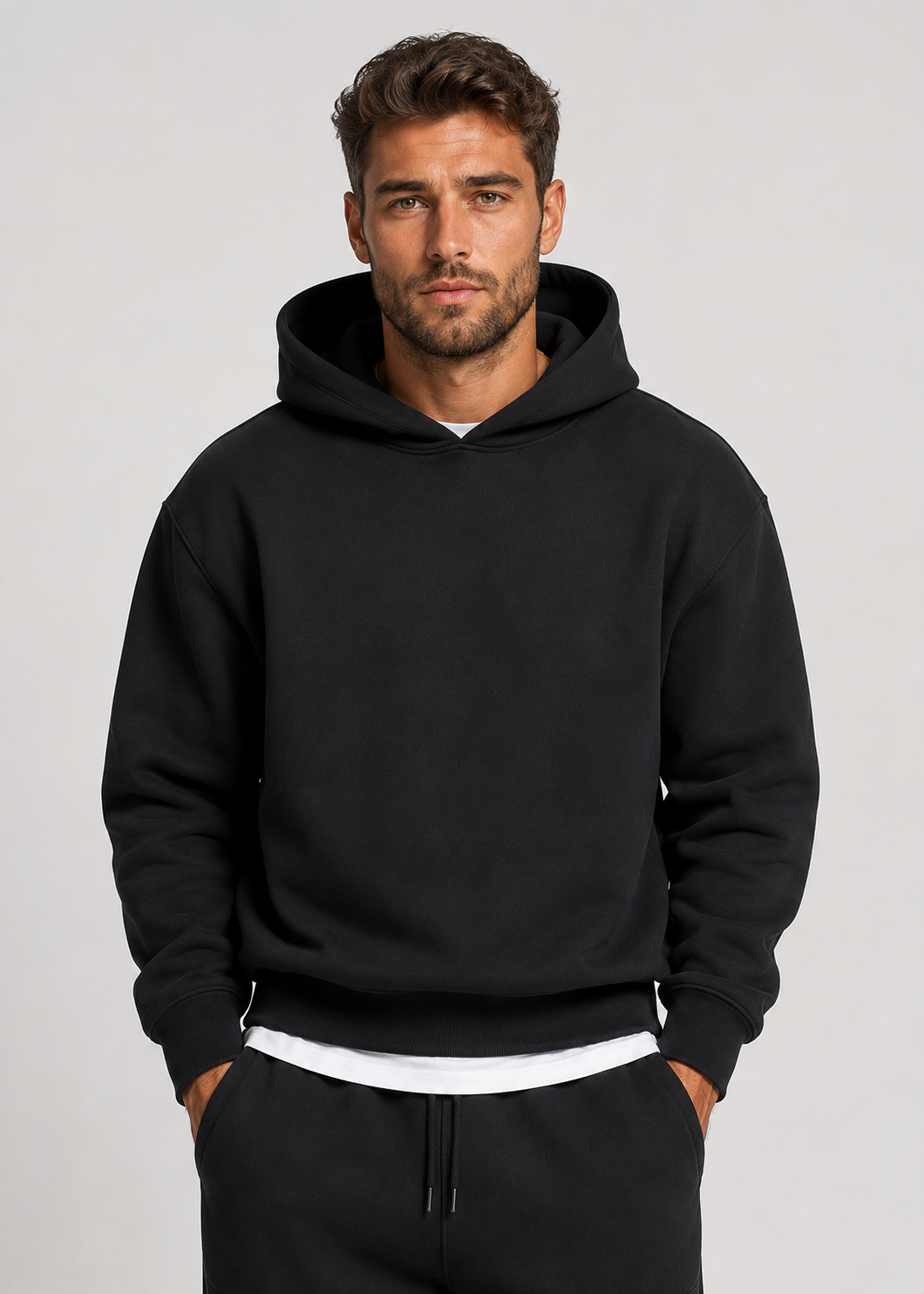 Close front view of the black hooded sweatshirt on a model, showing the ribbed cuffs and hem over a white layer. 2