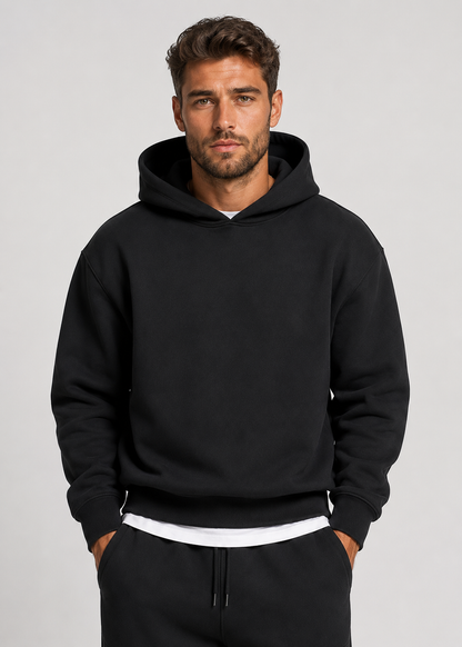 Close front view of the black hooded sweatshirt on a model, showing the ribbed cuffs and hem over a white layer. 2