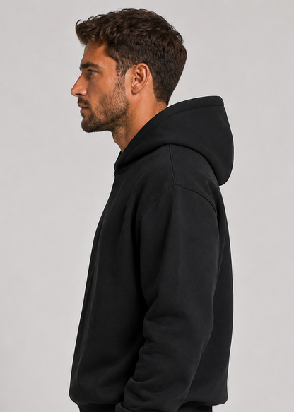 Side profile of the black hoodie on a model, showing the roomy hood, dropped shoulder seam and sleeve shape. 3
