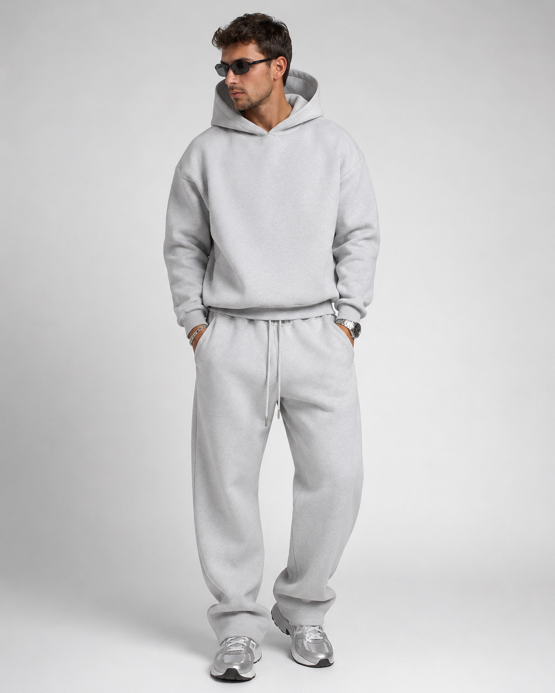 Studio shot of a model in the light grey marl hoodie and drawstring joggers, wearing sunglasses and silver trainers. 13