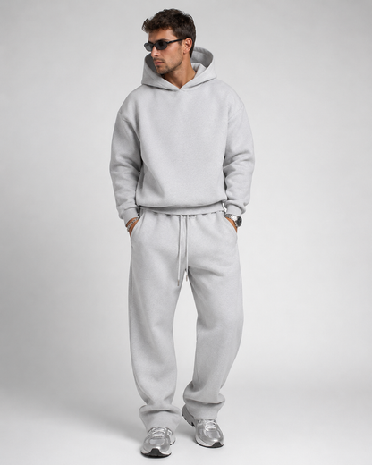 Studio shot of a model in the light grey marl hoodie and drawstring joggers, wearing sunglasses and silver trainers. 13