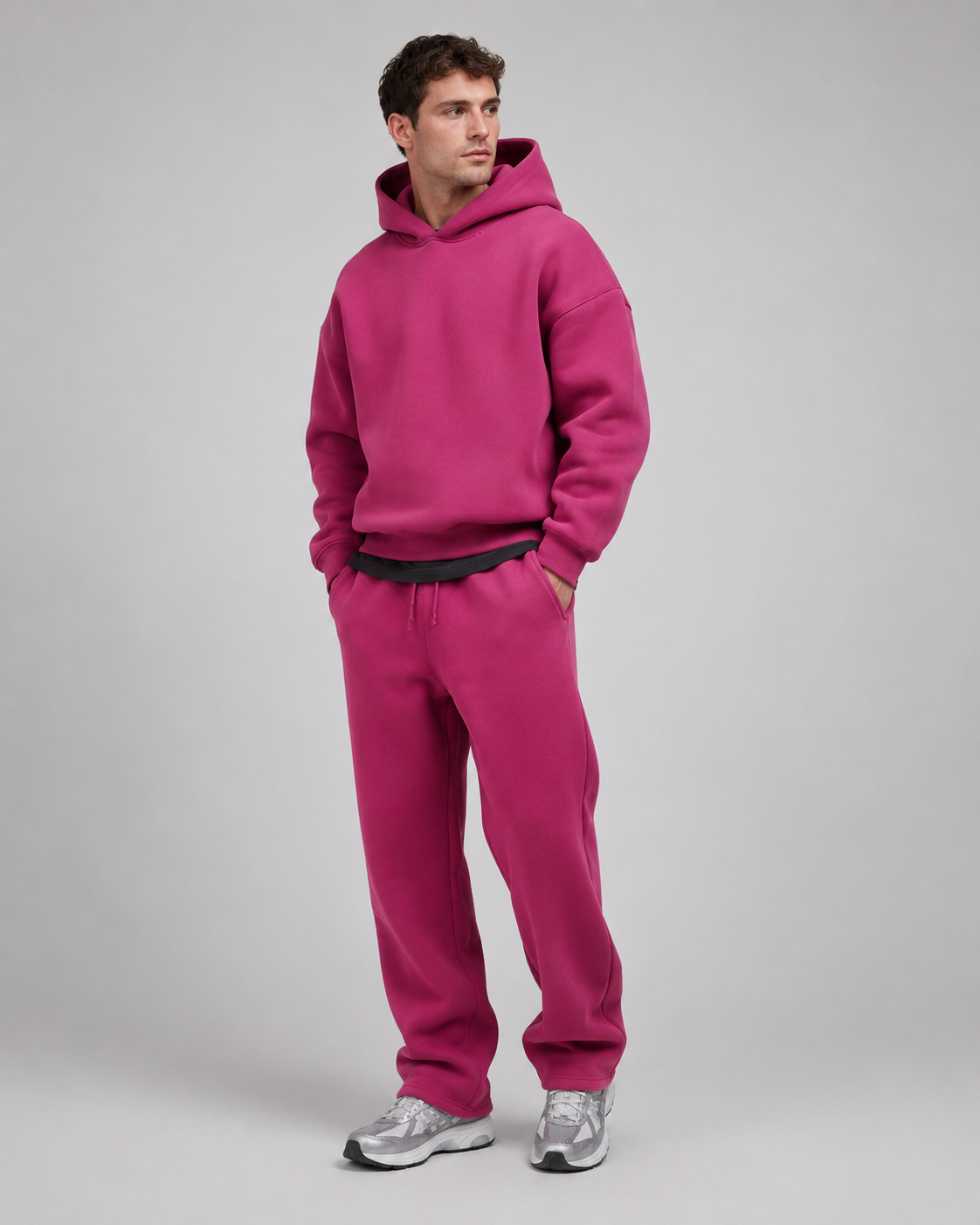 Studio shot of a model in the magenta pink hoodie and joggers, with a dark layer underneath and silver-grey trainers. 11