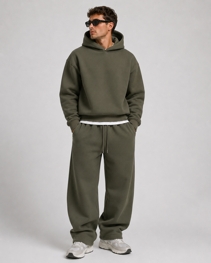 Studio shot of a model in the dark olive green hoodie and baggy joggers, wearing sunglasses and off-white trainers. 10