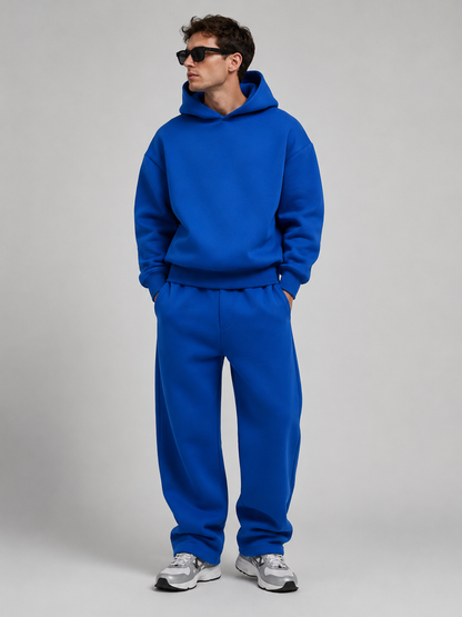 Studio shot of a model in the royal blue hoodie and wide-leg joggers set, wearing sunglasses and grey and white trainers. 8