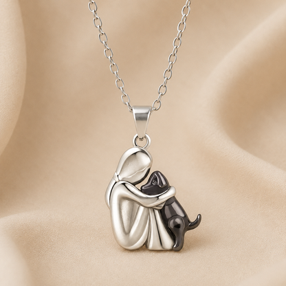 Pendant with a silver-toned seated figure holding a black dog, shown on soft beige fabric 3