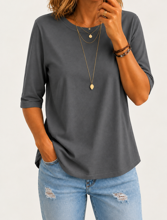 Close-up of a model in a dark grey round-neck half-sleeve tee, layered gold necklaces and ripped light jeans, against a plain light backdrop. 1