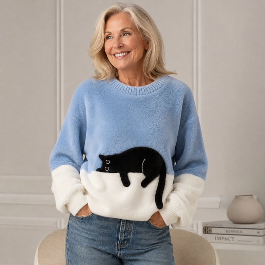 Smiling woman with blonde hair wears the fluffy light blue and white jumper with a black cat, hands in jeans pockets. 1