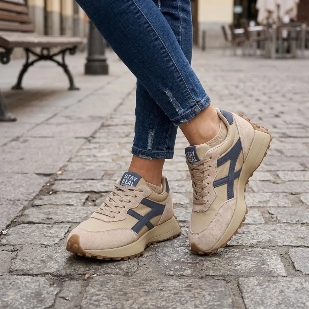Beige trainers with navy stripes worn with distressed jeans on a cobbled street 2