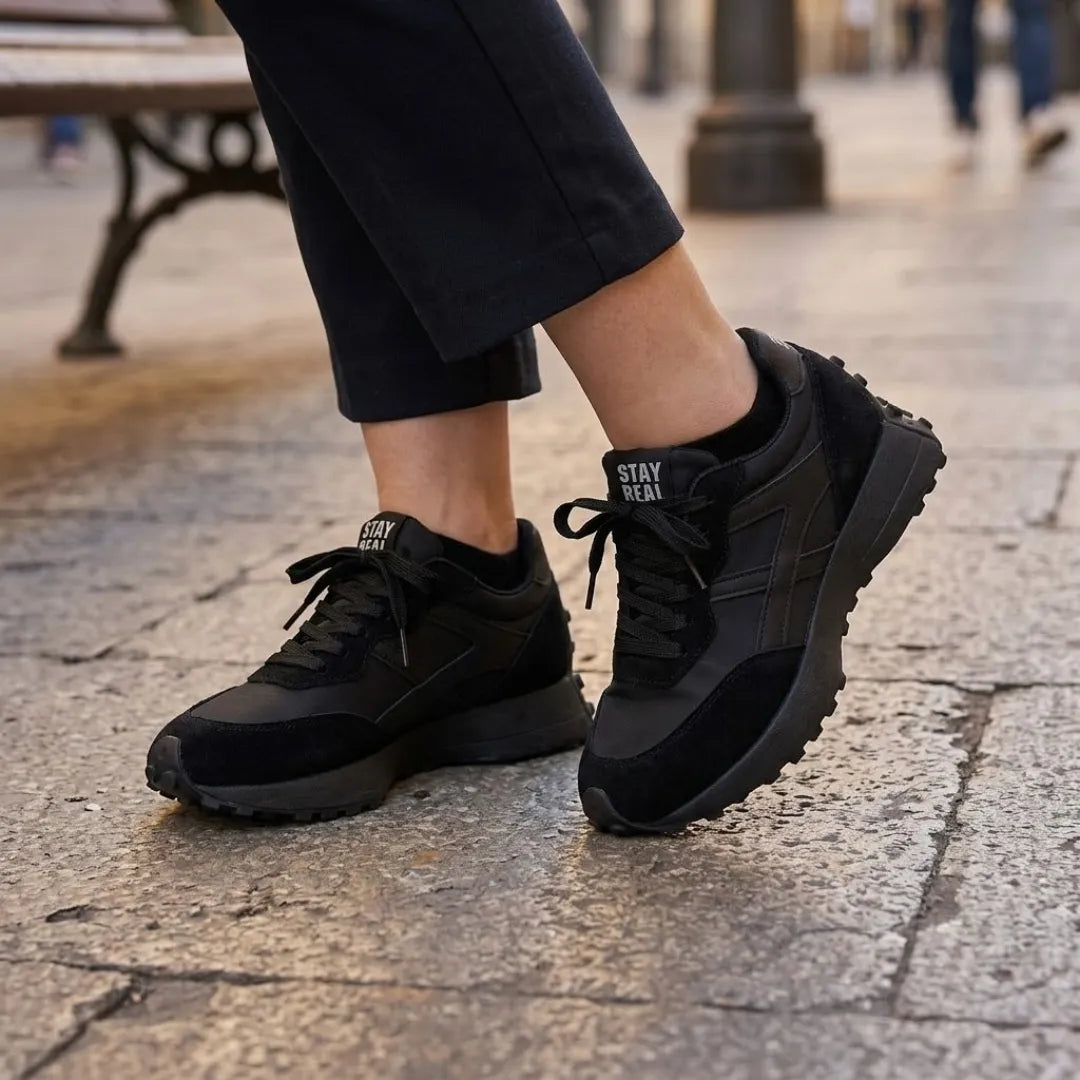 Black trainers with black laces worn with dark cropped trousers on a paved street 7