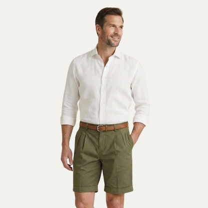 Man glancing aside, wearing olive green pleated turn-up shorts with a tan belt and a white linen shirt. 12