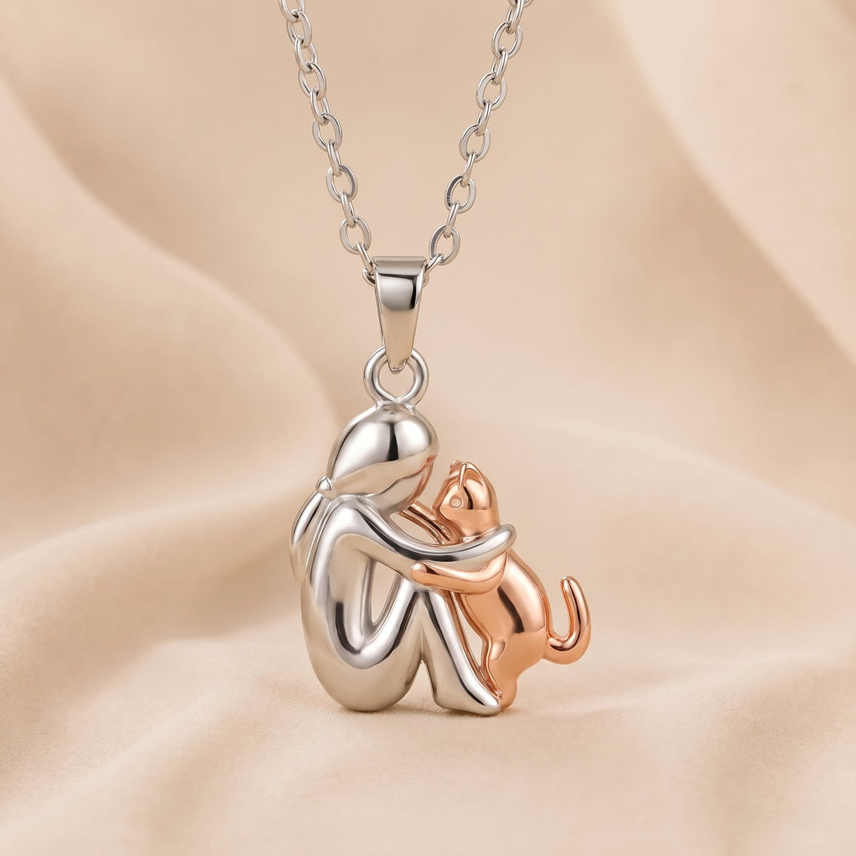 Polished silver-toned figure embracing a rose-gold-toned cat that reaches up, on a peach cloth backdrop 4