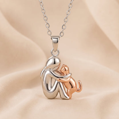 Polished silver-toned figure embracing a rose-gold-toned cat that reaches up, on a peach cloth backdrop 4