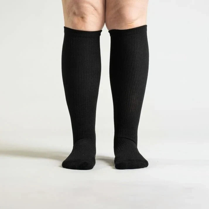 Front view of a model standing in black knee-high ribbed socks that reach just below the knee. 3