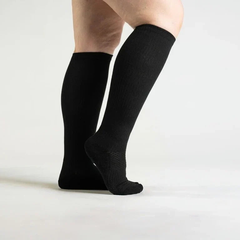 Side view of a model wearing black knee-high ribbed socks, one foot raised to show the textured cushioned sole. 1