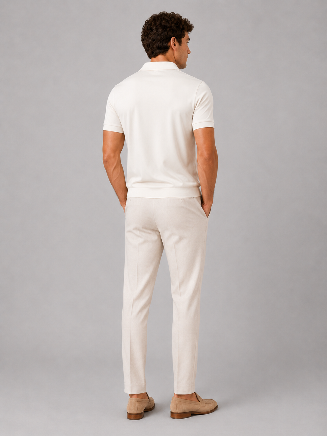 Back view of the model wearing the cream polo, showing the plain back, ribbed hem and short sleeves with pale trousers and loafers. 24
