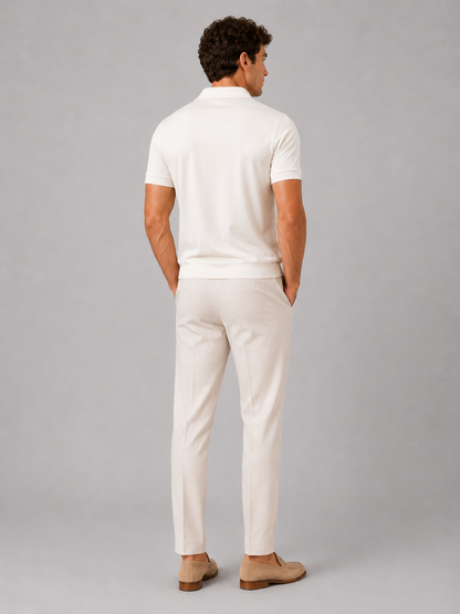 Back view of the model wearing the cream polo, showing the plain back, ribbed hem and short sleeves with pale trousers and loafers. 24