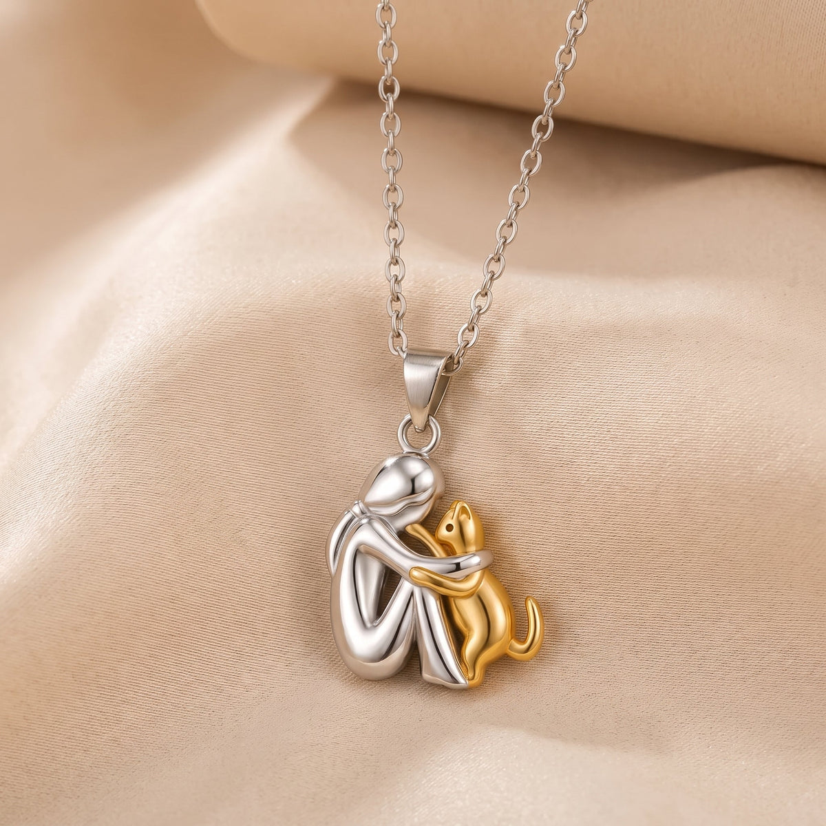 Polished pendant of a seated figure hugging a gold-toned cat, hanging from a fine chain on satin 2
