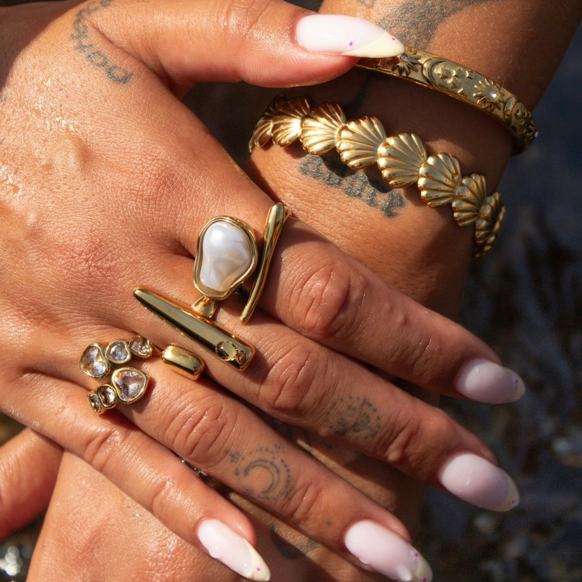 Close-up of a hand wearing the bar ring stacked with a pearl ring, a gem-set ring and gold bracelets. 3