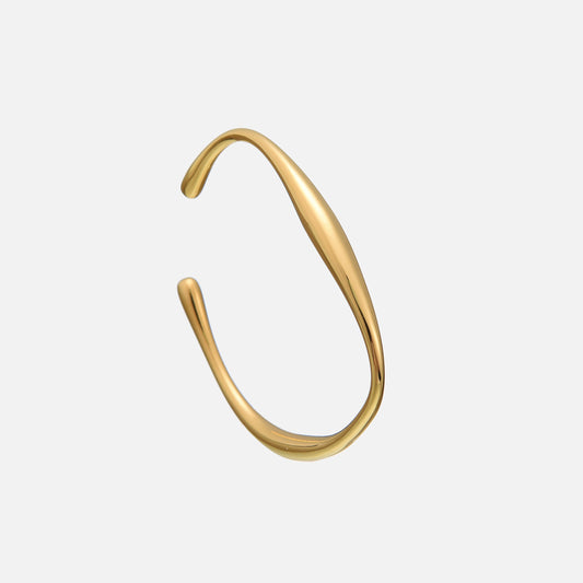 Open gold-coloured cuff bracelet with a smooth, flowing wave shape and rounded teardrop ends, shown at an angle on a plain grey background. 1