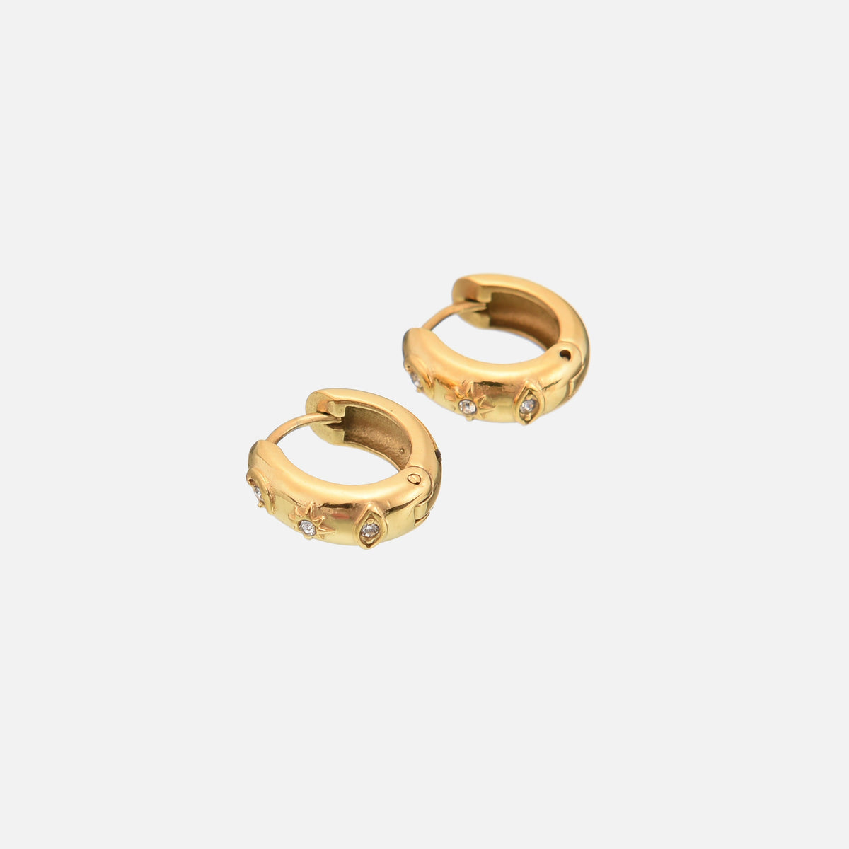 Two gold-tone chunky huggie hoops angled together on a light background, showing their hinged closure and the small clear stones set in the star and eye motifs. 2