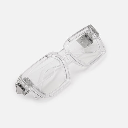 Folded clear acrylic glasses with silver hinge detail, shot at an angle to show the thick square frame and temple arms. 22