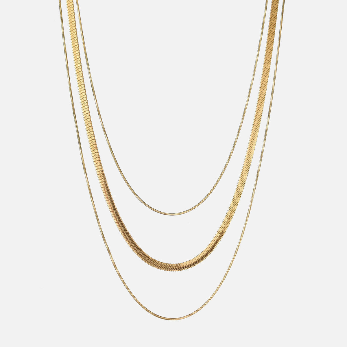 Three gold-toned chains of different widths hanging in layers against a plain light background 1